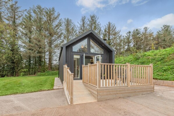 A modern cabin with a wooden deck, surrounded by trees.