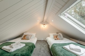 A cozy attic bedroom with two beds, a skylight, and a small window.