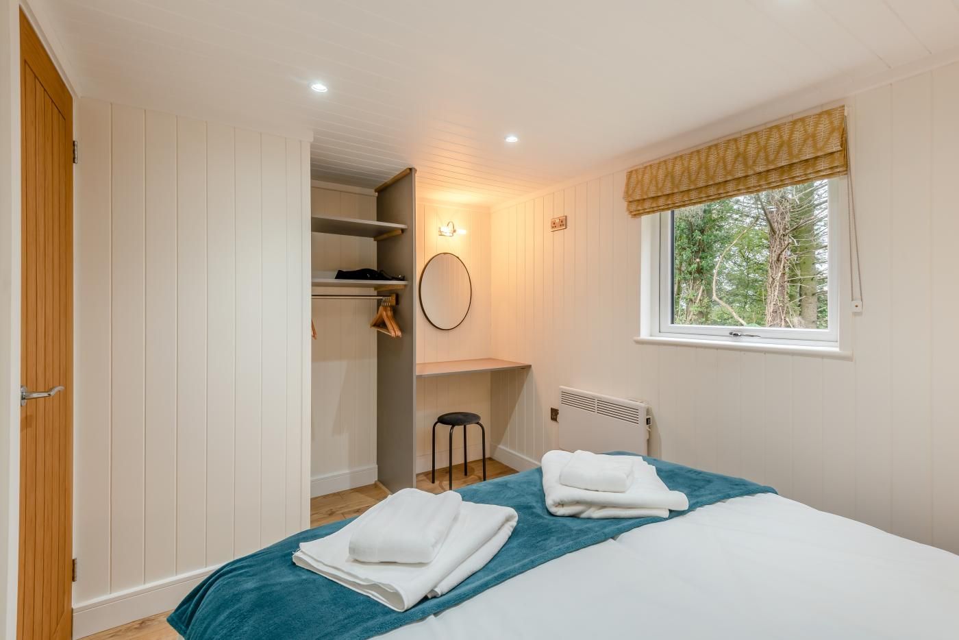 Een slaapkamer met een bed, een raam met uitzicht op bomen, een inbouwkast en een radiator.