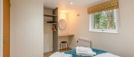 Een slaapkamer met een bed, een raam met uitzicht op bomen, een inbouwkast en een radiator.