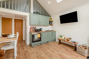 A compact kitchen with a dining area, wooden flooring, and a TV mounted on the wall.