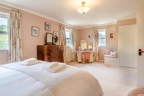 Quarto com cama grande, cômoda, escrivaninha e janela com cortinas.