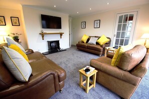 Ein Wohnzimmer mit braunen Ledersofas, einem Wand-Fernseher, einem Kamin und einer Tür mit Glasfeldern.