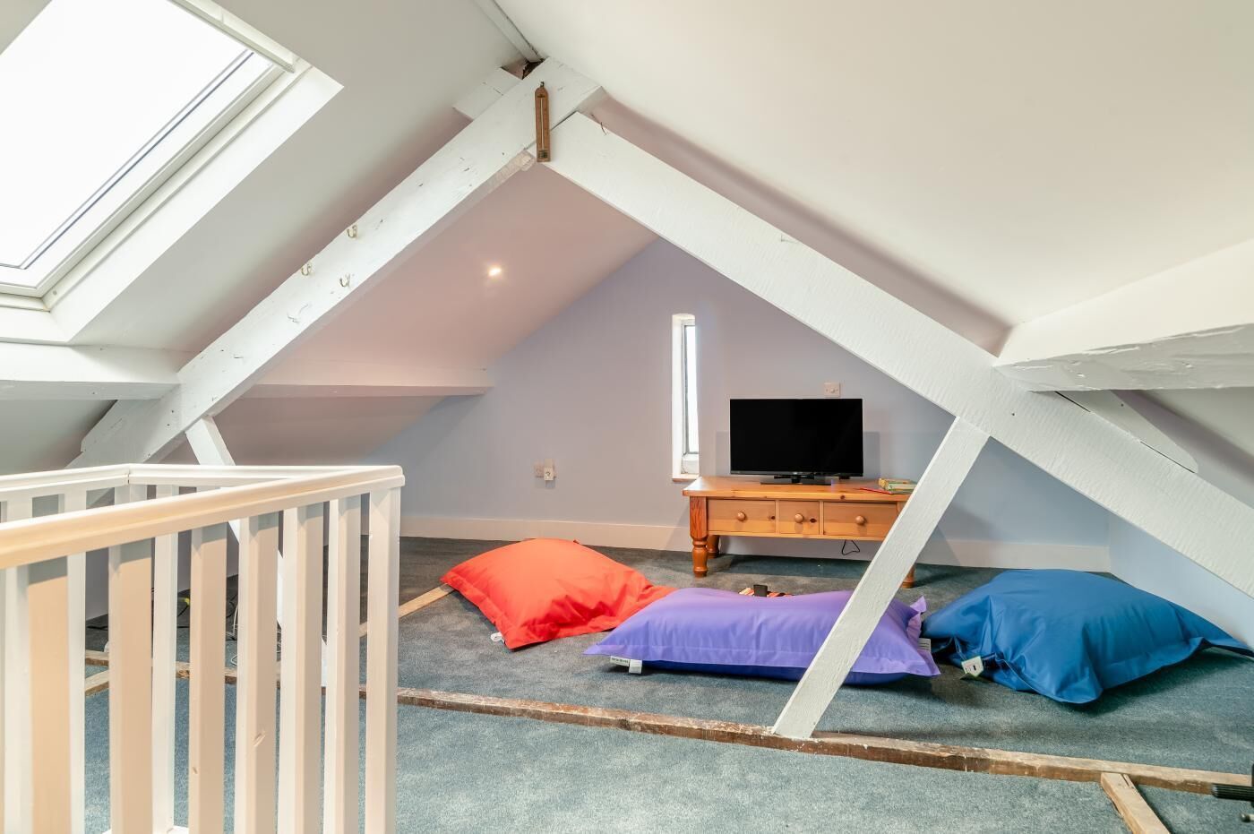 Une chambre mansardée avec un plafond en pente, une commode en bois, un téléviseur et une petite fenêtre.