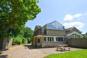 A two-story stone house with a large glass conservatory, a wooden fence, and a picnic table in the yard. - 2 Bed in Cardiff (oc-45378) (Peterston-super-Ely)