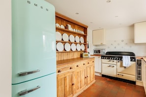 A kitchen with a teal refrigerator, wooden cabinets, a stove, and a microwave. - 3 Bed in Burton Bradstock (oc-c33542) (Burton Bradstock)