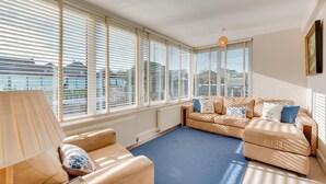 A spacious living room with a large window, a sofa set, and a lamp. - 4 Bed in Old Hunstanton (oc-1809) (Hunstanton)