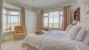 A bedroom with a large bed, a chair, and a wardrobe. - 4 Bed in Old Hunstanton (oc-1809) (Hunstanton)