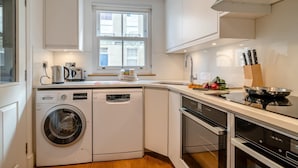 A compact kitchen with a Bosch washing machine, a toaster, and a window with a view of buildings. - 2 Bed in Bath (oc-bhr44) (Bath)