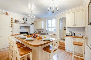 A well-lit kitchen with white cabinetry, a wooden dining table, and chairs. There are two windows providing natural light, and a chandelier hangs from the ceiling. - 4 Bed in Whitby (oc-w414) (Whitby)