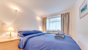 A bedroom with a bed, bedside table, lamp, window with curtains, and a painting on the wall. - 1 Bed in Saundersfoot (oc-pw9247) (Saundersfoot)