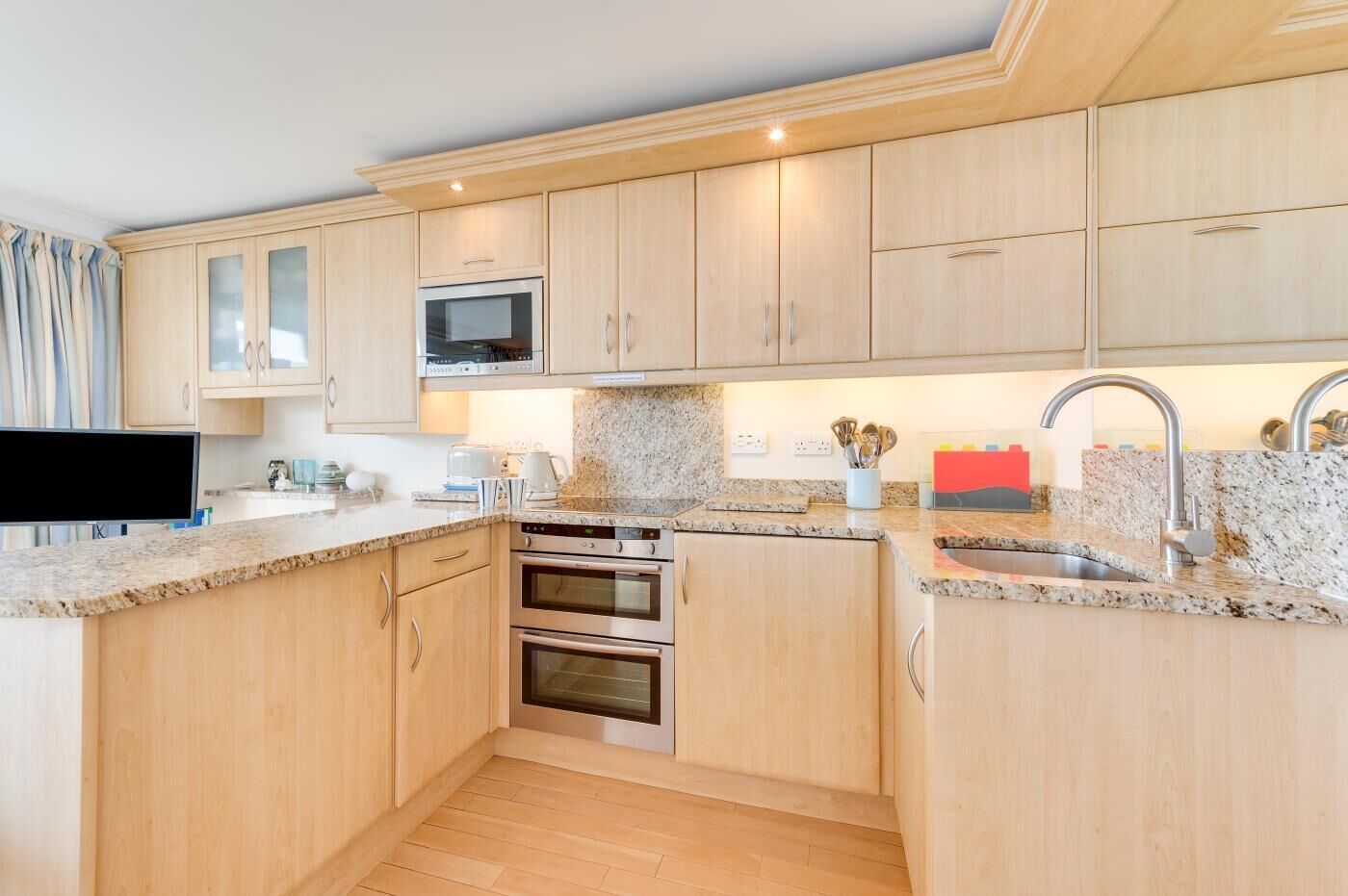 A modern kitchen with wooden cabinets, a microwave, two ovens, granite countertops, and a stainless steel sink.