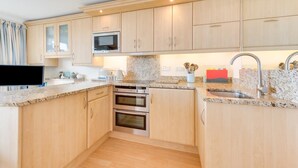 A modern kitchen with wooden cabinets, a microwave, two ovens, granite countertops, and a stainless steel sink. - 1 Bed in Saundersfoot (oc-pw9247) (Saundersfoot)