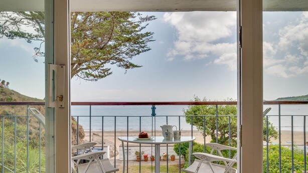 A balcony with a view of the beach, a table with chairs, and a small garden area. - 1 Bed in Saundersfoot (oc-pw9247) (Saundersfoot)