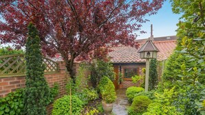 A brick house with a tiled roof, a wooden gate, and a garden with various plants and a tree with red leaves. - 1 Bed in Redcar (oc-cl003) (Redcar)