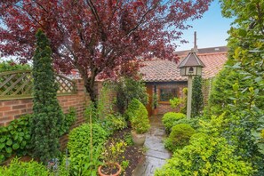 A brick house with a tiled roof, a wooden gate, and a garden with various plants and a tree with red leaves. - 1 Bed in Redcar (oc-cl003) (Redcar)