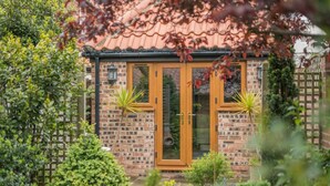 A brick building with a tiled roof, a wooden door, and two potted plants. - 1 Bed in Redcar (oc-cl003) (Redcar)