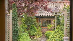 A traditional Japanese-style house with a tiled roof, a wooden window, and a small garden with various plants and a stone pathway. - 1 Bed in Redcar (oc-cl003) (Redcar)