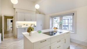 Une cuisine moderne avec des meubles blancs, un grand îlot central doté d’une plaque de cuisson intégrée et une fenêtre offrant une vue sur la ville.
