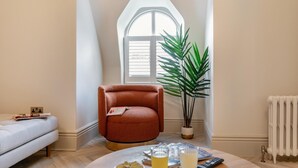 A cozy living room with a high ceiling, a red armchair, a potted plant, a radiator, and a window with blinds. - 3 Bed in Buxton (oc-c33947) (Buxton)