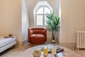 Un salón acogedor con techo alto, un sillón rojo, una planta en maceta, un radiador y una ventana con persianas.