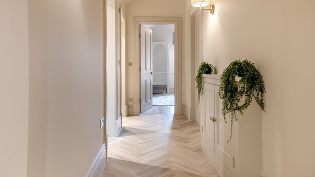 A hallway with a herringbone floor, white walls, and a door leading to another room. - 3 Bed in Buxton (oc-c33947) (Buxton)