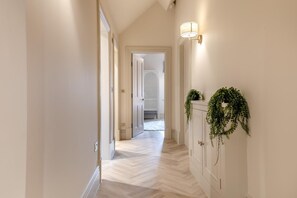 Un couloir doté d’un parquet en point de Hongrie, de murs blancs et d’une porte donnant sur une autre pièce.