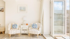 A room with two striped armchairs, a small white table, a white lamp, and a glass door leading outside. - 4 Bed in Little Petherick (oc-urchpe) (Little Petherick)