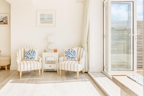 Una habitación con dos sillones a rayas, una pequeña mesa blanca, una lámpara blanca y un ventanal de vidrio que da al exterior.