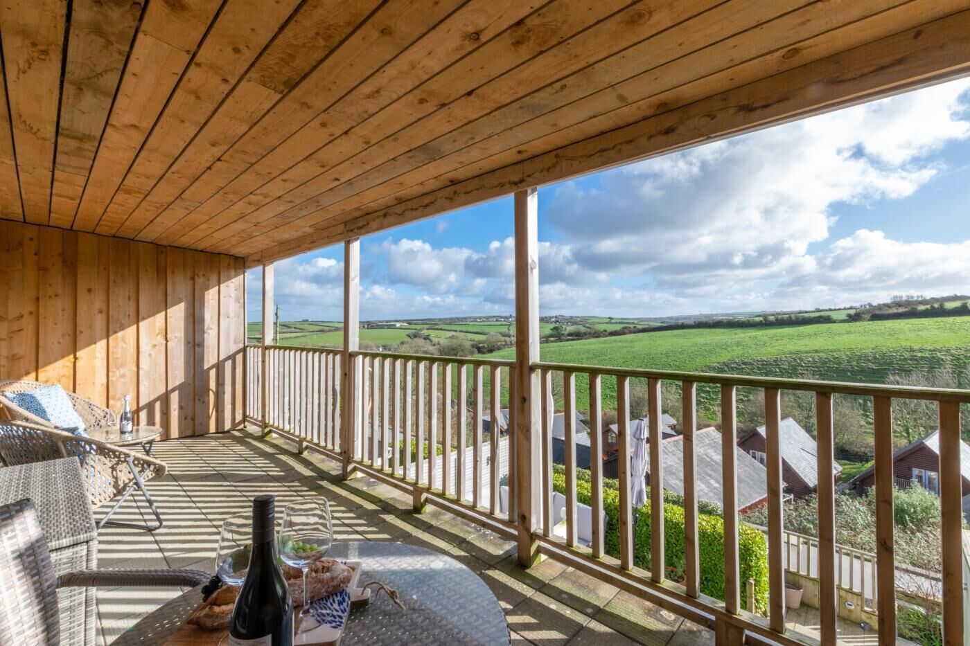 Un balcon en bois offrant une vue sur des champs verdoyants et des maisons.