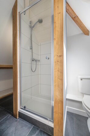 Une douche avec une porte en verre, une poutre en bois et des toilettes blanches dans une salle de bain moderne.