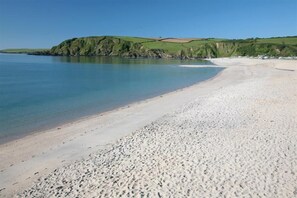 A beach with clear blue water, sandy shore, and green hills in the background. - 4 Bed in Pentewan (oc-edghil) (Pentewan)