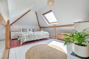 Une chambre avec un puits de lumière, un lit avec une literie à motifs floraux, une table de chevet, une commode, une armoire en bois et une plante en pot.