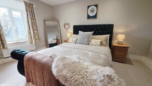 A bedroom with a large bed, two bedside tables, a mirror, and a window with curtains.