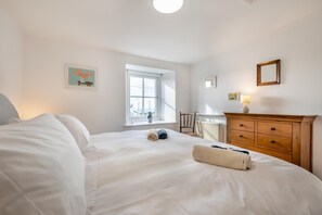 Een slaapkamer met een groot bed, een houten dressoir, een raam met uitzicht en een kleine tafel met een lamp.