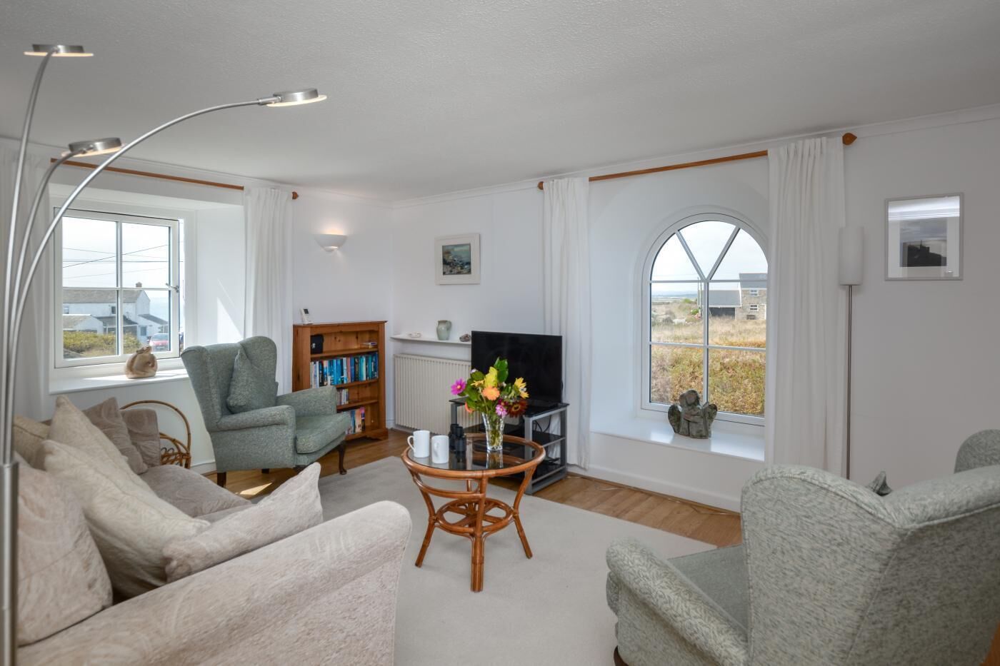 A living room with a sofa, armchairs, a bookshelf, a TV, and a large window with a view.
