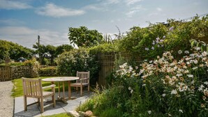 Une terrasse avec une table ronde et deux chaises, entourée d’une végétation luxuriante et de plantes en fleurs.
