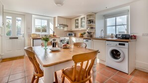 Une cuisine moderne avec un coin repas, des meubles blancs, un lave-linge et une grande fenêtre.
