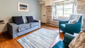 Ein Wohnzimmer mit grauem Sofa, blauem Sessel, Teppich mit Muster, Steinwand und Fenster mit Blick.