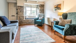 Ein gemütliches Wohnzimmer mit Steinwand, Fenster mit Blick, blauem Sessel und grauem Sofa.