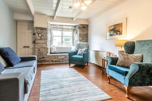 Ein gemütliches Wohnzimmer mit Steinwand, Fenster mit Blick, blauem Sessel und grauem Sofa.