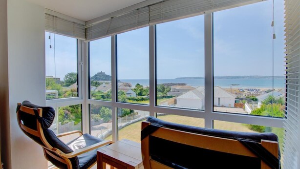 A balcony with large windows overlooking a coastal area, furnished with two chairs and a small table. - 4 Bed in Marazion (oc-gwynsa) (Marazion)