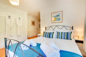 A hotel room with a bed, towels, a metal chair, a painting, and a wardrobe with robes. - 4 Bed in Marazion (oc-gwynsa) (Marazion)