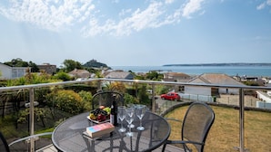 A balcony with a table set for two, a red car in the background, and a view of the sea and buildings. - 4 Bed in Marazion (oc-gwynsa) (Marazion)