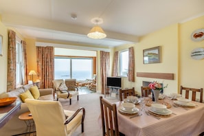 A dining area with a table set for four, a television, and a view of the sea. - 3 Bed in Sennen (oc-cpz56) (Sennen)