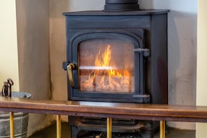 A wood-burning stove with a glass door, a metal handle, and a metal grate below. - 3 Bed in Sennen (oc-cpz56) (Sennen)