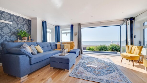 A modern living room with a blue sofa, a yellow armchair, and a large window offering a view of the sea.