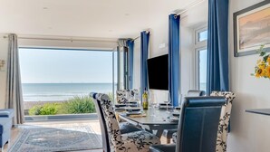 A dining area with a view of the sea, a table set for four, and blue curtains.