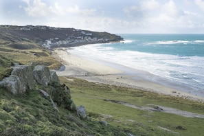 Eine Küstenlandschaft mit Strand, Felsen und einer entfernten Anhöhe mit Gebäuden.