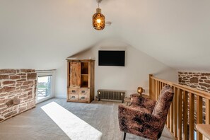 A loft bedroom with a sloped ceiling, exposed brick walls, a wooden wardrobe, a leopard print chair, and a hanging light fixture. - 3 Bed in Wigton (oc-f33746) (Westward)